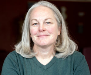 Alexis Hart is facing viewer, smiling, wearing a green top posing in front of a dark background.
