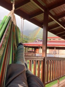 photo showing legs and feet in a hammock on a balcony looking out over mountains with a rainbow in the distance.