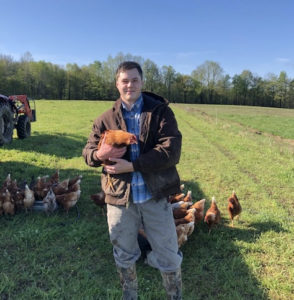 Allegheny College student Brandon Bolling holding a live chicken in a farm field