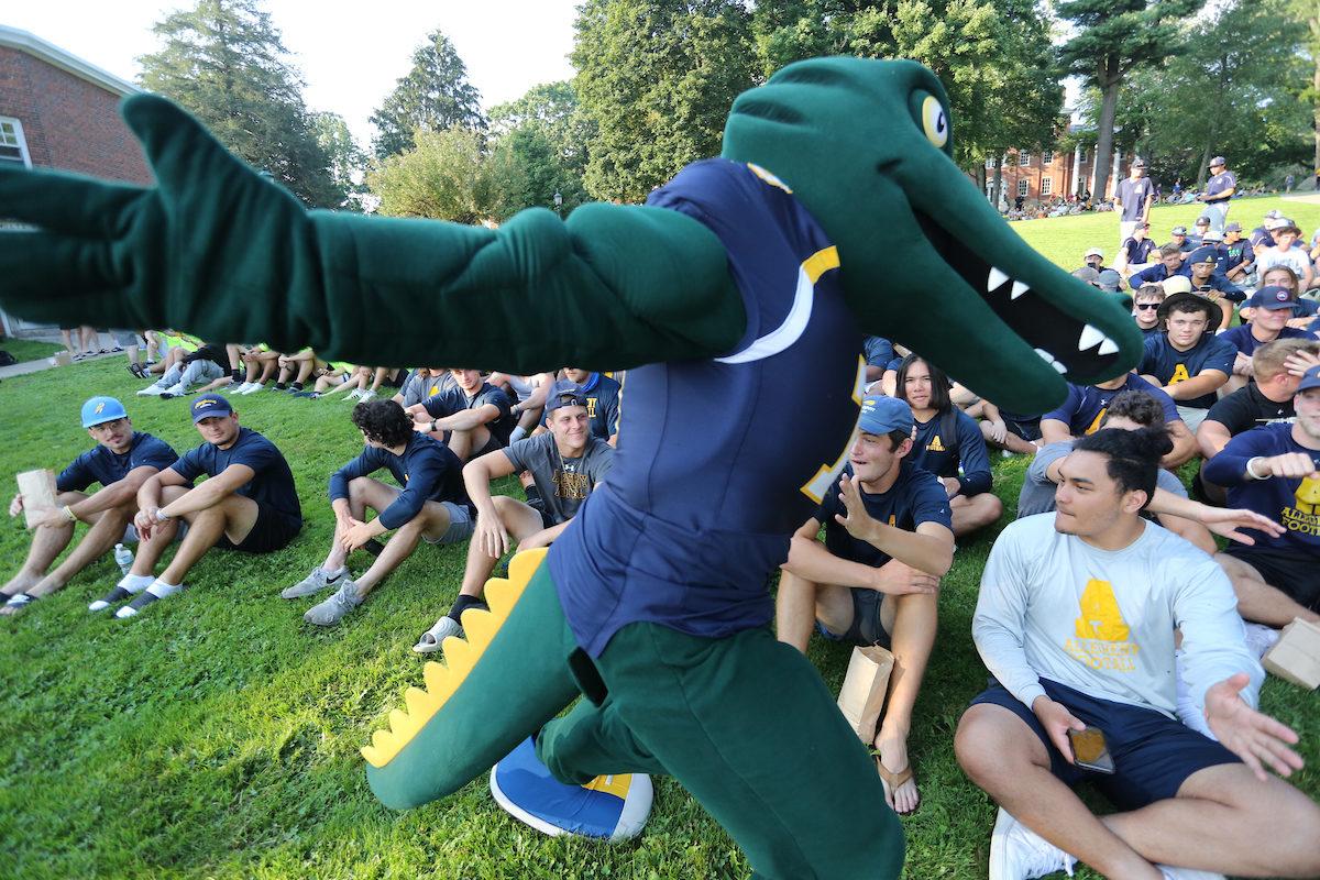 Chompers the mascot greets students sitting on the grass
