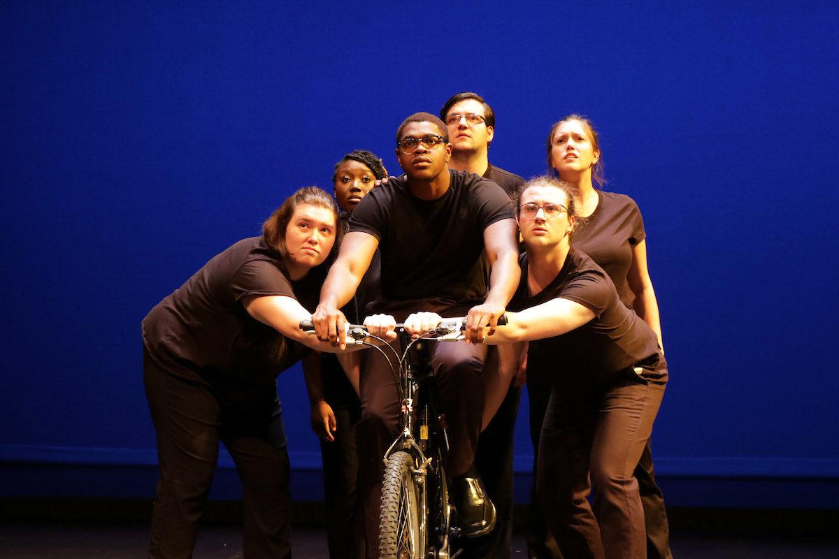 a student actor on a bicycle, surrounded by other students