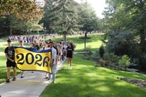 A line of students processes to the Matriculation ceremony. Students in the front hold a blue and yellow banner with "2026."