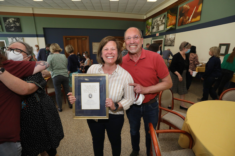 two individuals smile, with one holding a framed award
