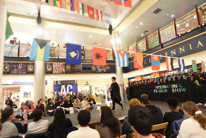 student walks on a stage with several countries flags hanging above and audience members looking on