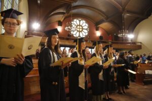 Students wearing regalia hold pamphlets and sing in a chapel